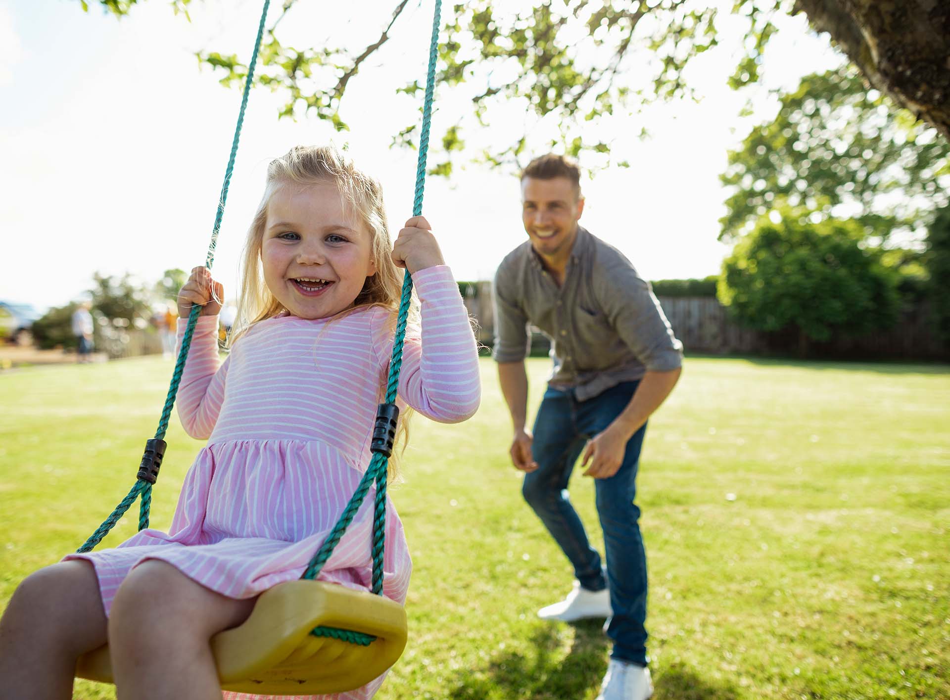 Der Anschwung zum eigenen Spielparadies Vater gibt der Schaukel anschwung auf dem seine kleine lächelnde Tochter sitzt