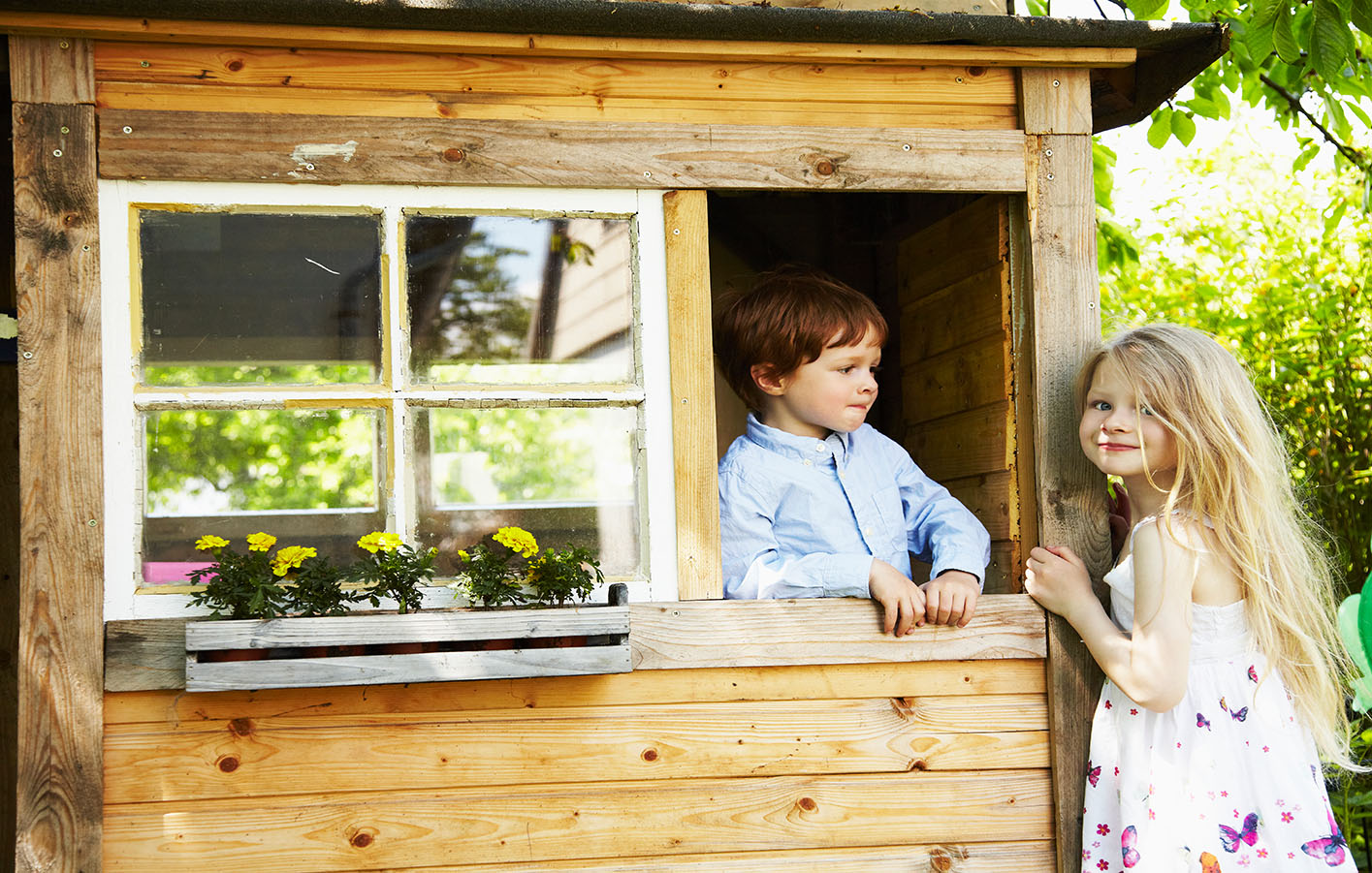 Mädchen und Junge in einem Spielhaus aus Holz.